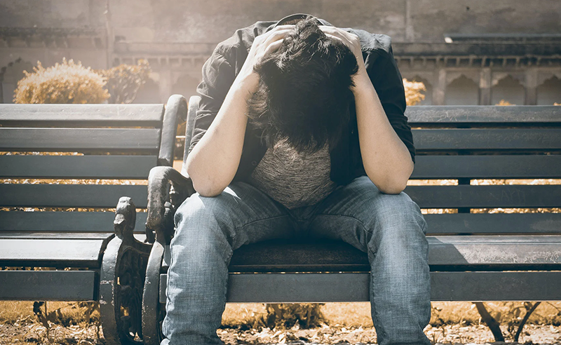 Male sitting on a bench with hands over head and a bike